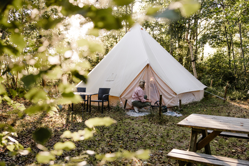 Bell tent met picknicktafel op een groene kampeerplek tussen de bomen